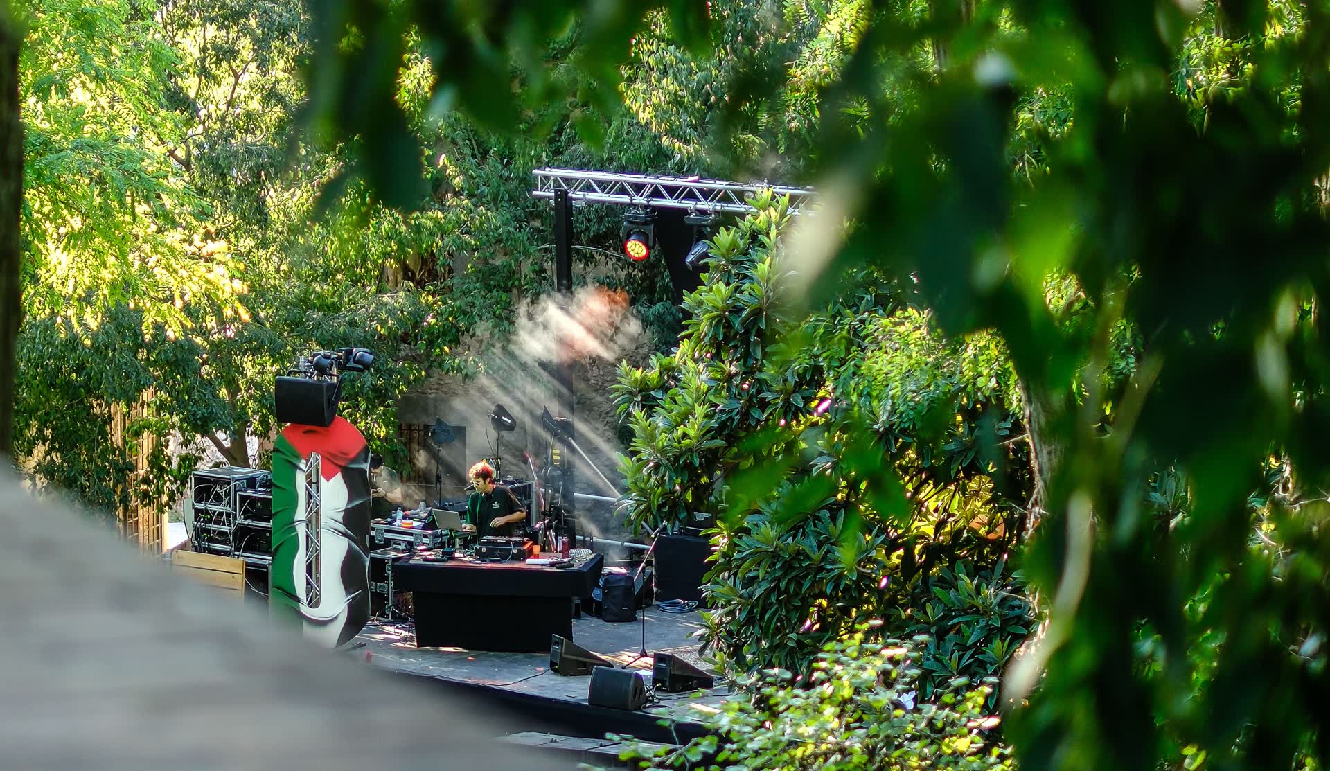 Muntatge de l'equip tècnic i de so en un escenari enjardinat, entre arbres, durant la preparació d'un concert