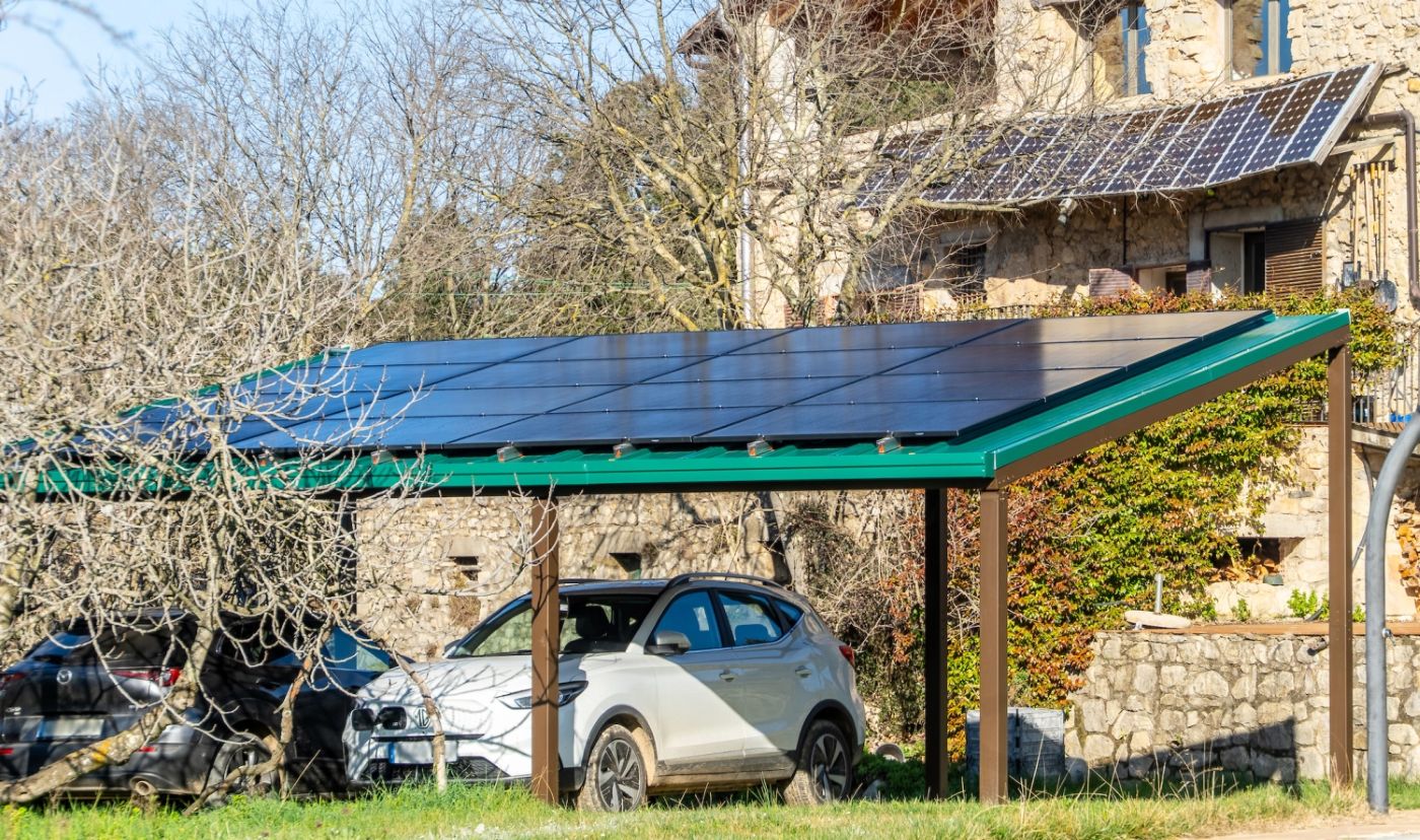L'estructura fent d'aparcament cobert al costat d'una casa de pedra